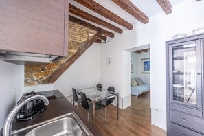 A modern kitchen with a glass dining table, wooden beams, and a stone wall.