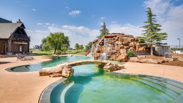 Ein Poolbereich mit Wasserfall, einer Brücke und einem Haus im Hintergrund.