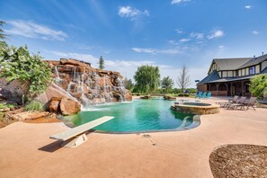 Una piscina con una cascata, una zona relax con sedie e un edificio con tetto a due falde.