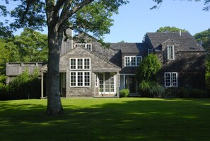 A two-story house with a large front lawn, a prominent tree, and a satellite dish.