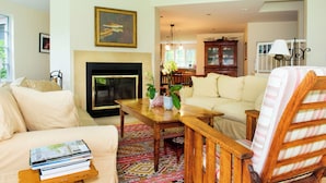 A living room with a fireplace, sofa, armchair, and a table with books. - Spacious and gracious architect designed home on 3 acres off Middle Road. (Chilmark)