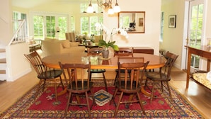 A spacious dining area with a large wooden table surrounded by chairs, a patterned rug, and a chandelier. - Spacious and gracious architect designed home on 3 acres off Middle Road. (Chilmark)