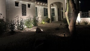 Un edificio blanco con techo de tejas, un camino de piedra y un árbol en primer plano.