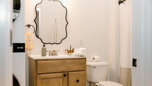 Une salle de bain avec un meuble-lavabo en bois, des toilettes blanches, un porte-serviettes et un miroir décoré d’un motif de bateau.