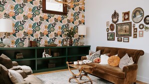 Un salon chaleureux avec un papier peint à motifs, un canapé marron, une table basse en bois et une bibliothèque verte.