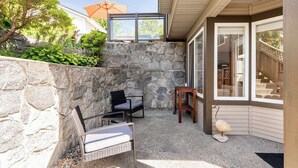 A patio with stone walls, a seating area with chairs, a small table, and a glass door leading to a covered area. - WestCoast Garden Suite | 1 Bedroom | Private | Quiet | Central | Modern (North Vancouver)