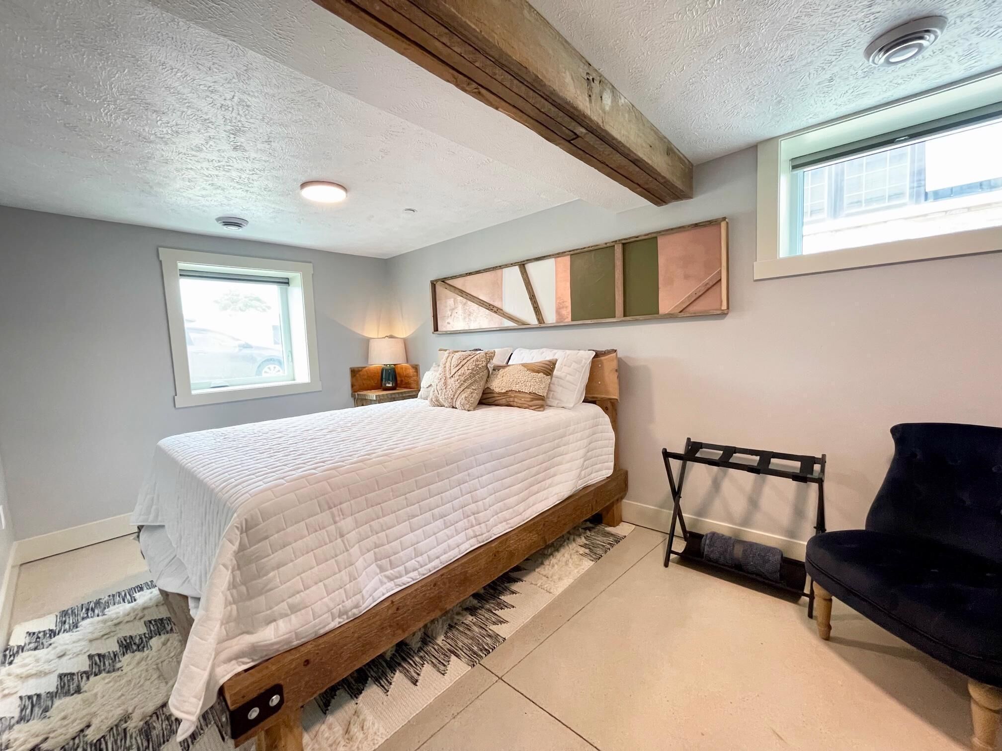 A bedroom with a wooden bed, a black chair, a rug, a lamp, and a painting on the wall.