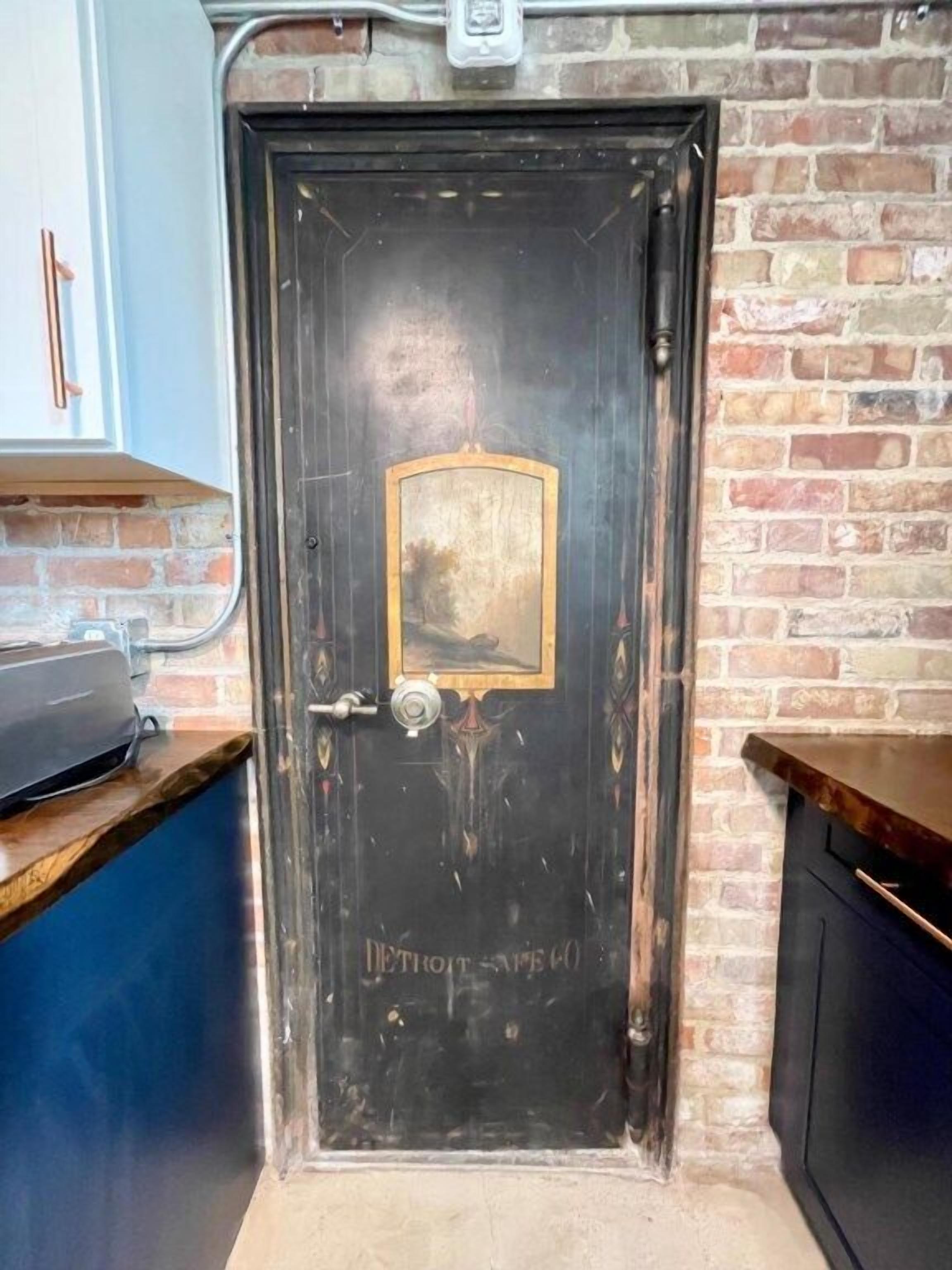 Une porte en bois sombre, dotée d’une poignée en laiton et d’une petite plaque en laiton portant l’inscription « Detroit Safe ».
