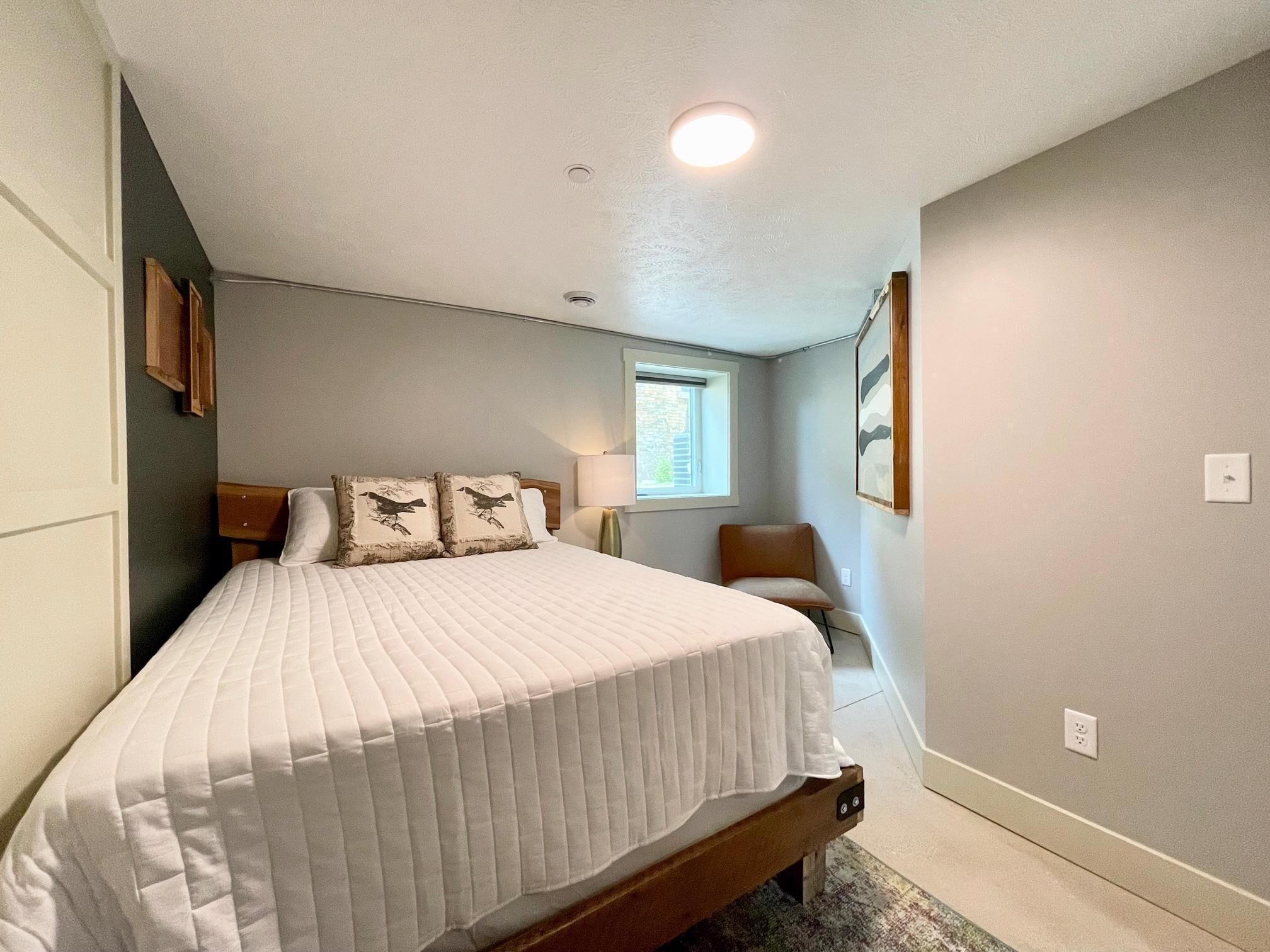A bedroom with a bed, a window, a chair, and a lamp.