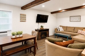 A living room with a wooden dining table, a sofa, a television mounted on the wall, and a fireplace.