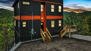 Une cabane à deux étages avec un mur d’accent rouge, un escalier en bois et une vue sur une chaîne de montagnes boisées.