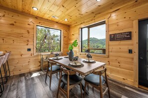 Interior de madeira com uma mesa de jantar posta para quatro pessoas, um vaso de planta e uma placa indicando que o local é o Parque Nacional das Montanhas Fumegantes.