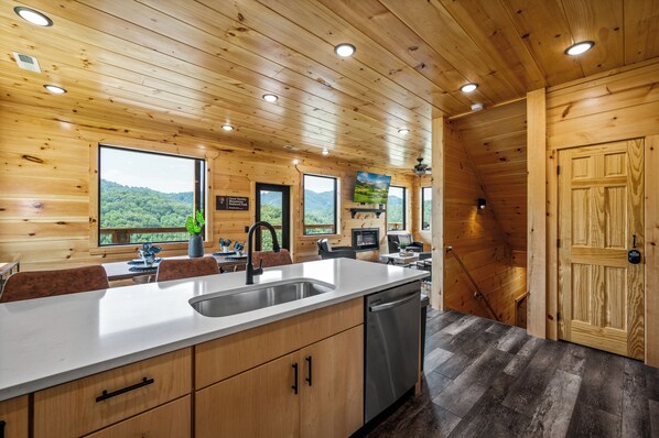 L’intérieur d’un chalet en bois comprend un coin cuisine, de grandes fenêtres et offre une vue sur la forêt.