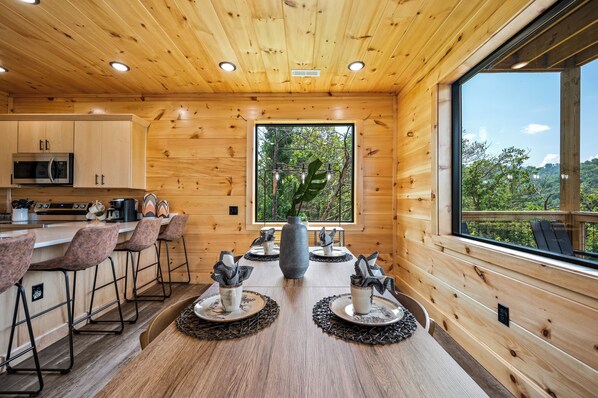 A modern kitchen with wooden walls, a large window, and a bar area with stools.