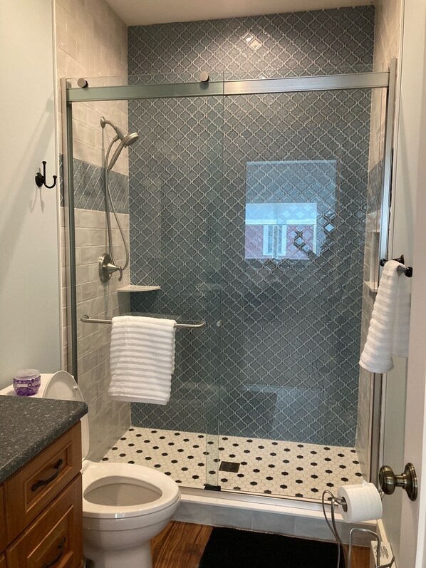 Et badeværelse med bruseniche, toilet, vask og håndklædestige.