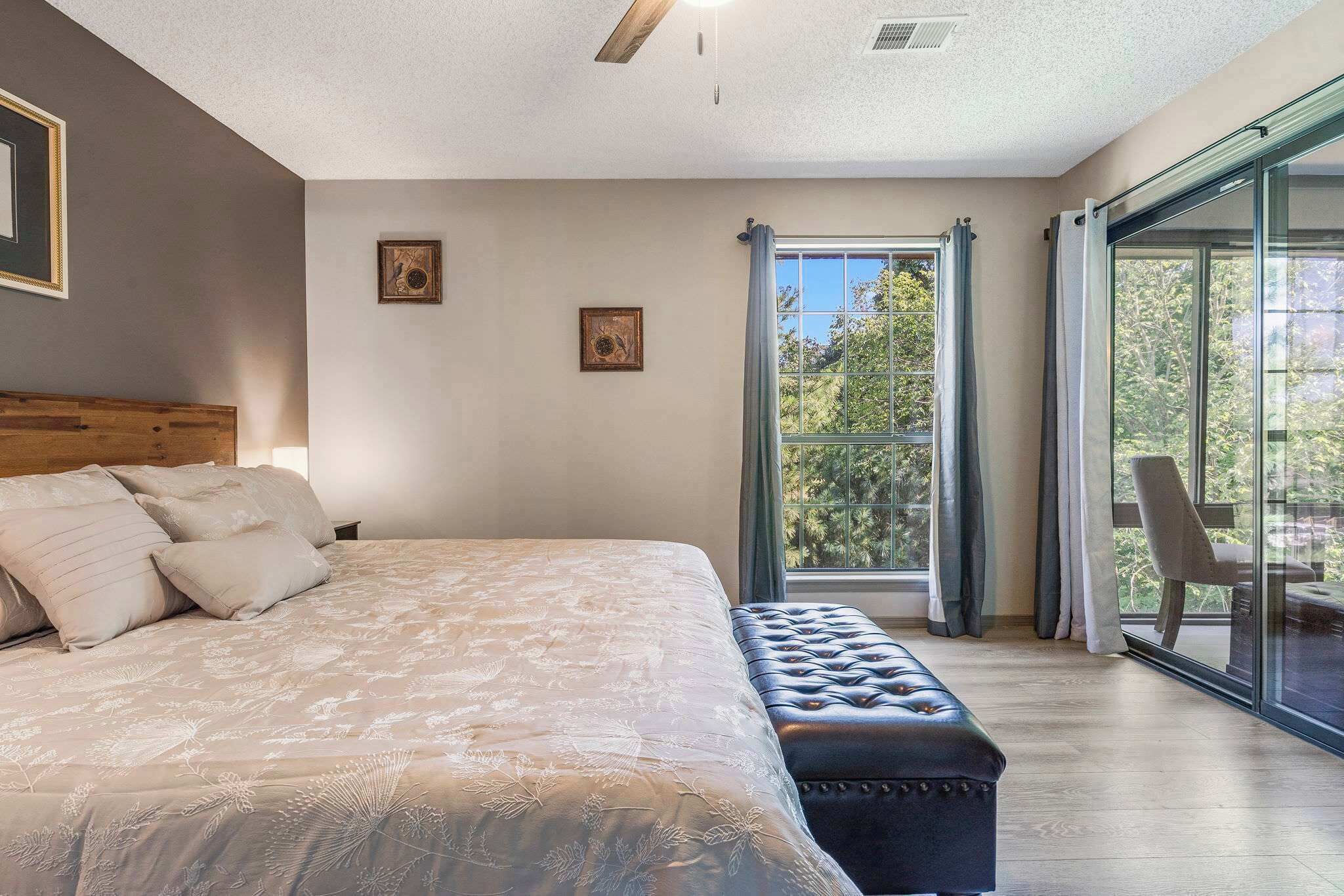 Un dormitorio con una cama grande, un banco, una ventana con cortinas y vistas a árboles.