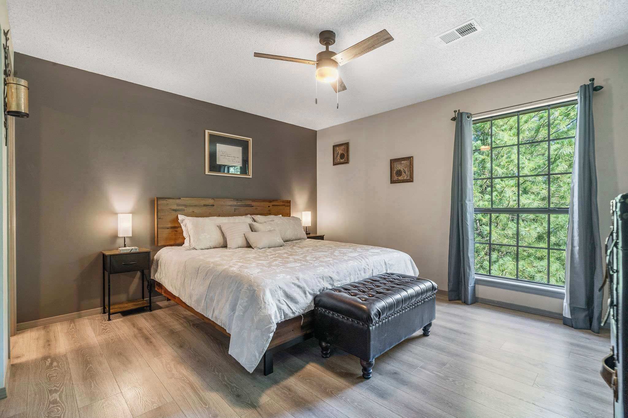 Un dormitorio con cama, mesita de noche y ventana con cortinas.