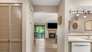 A hallway with a wooden door, a fireplace, a kitchen area with a dishwasher, and a large window. - Golf View Peek-a-boo (Branson)