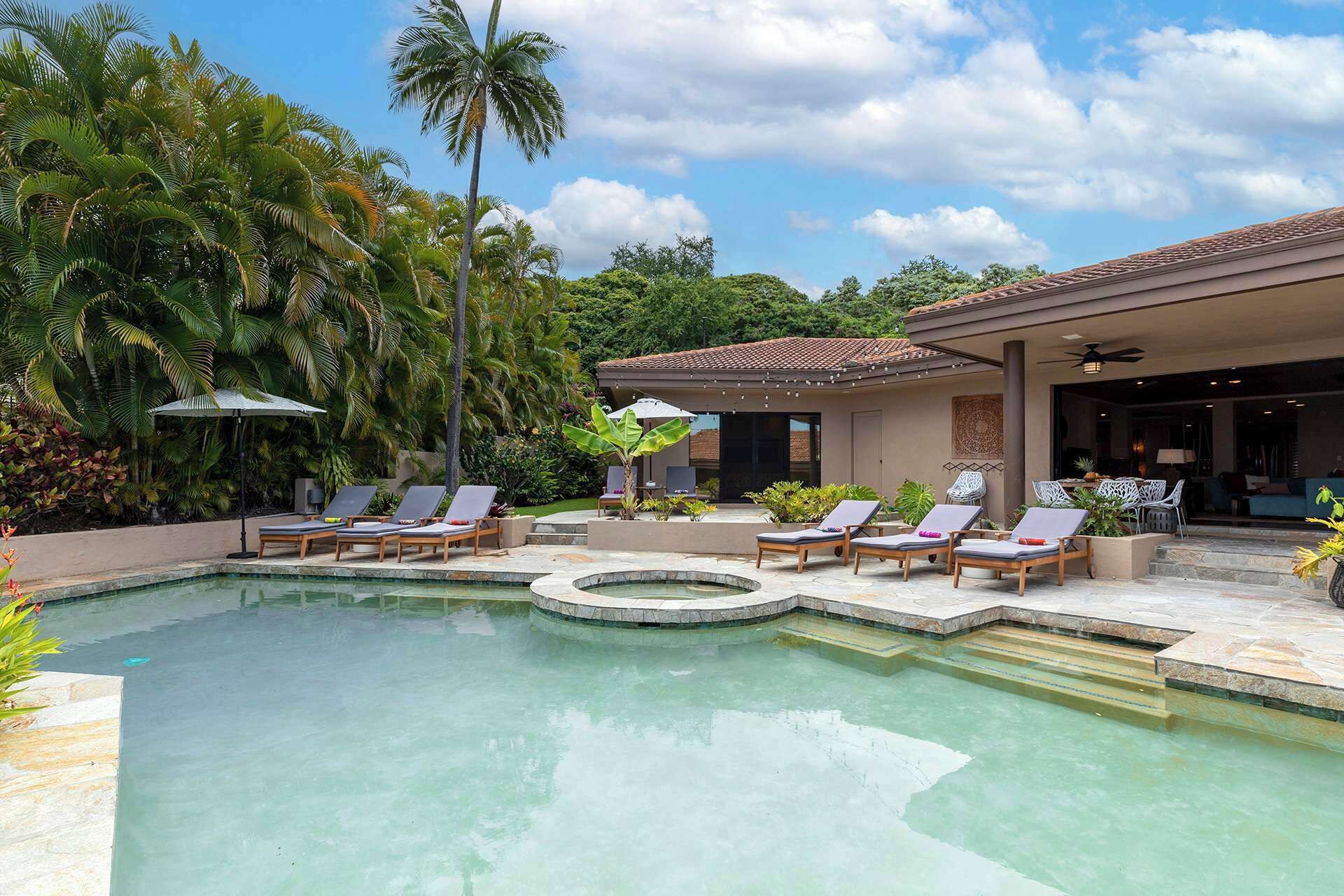 A pool area with lounge chairs, a covered seating area, and a building with a tiled roof.