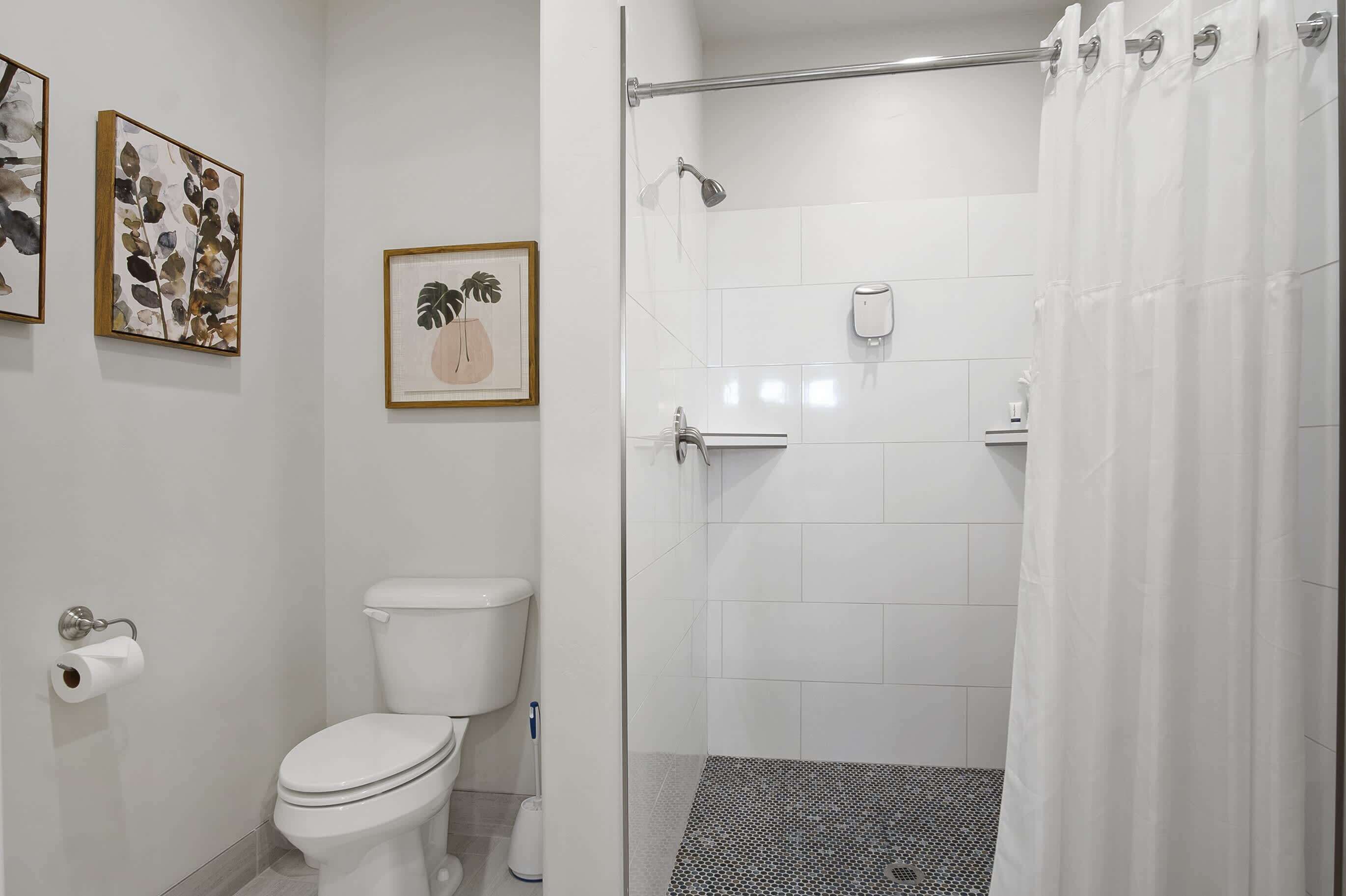 A modern bathroom with a toilet, shower, and toilet paper dispenser.