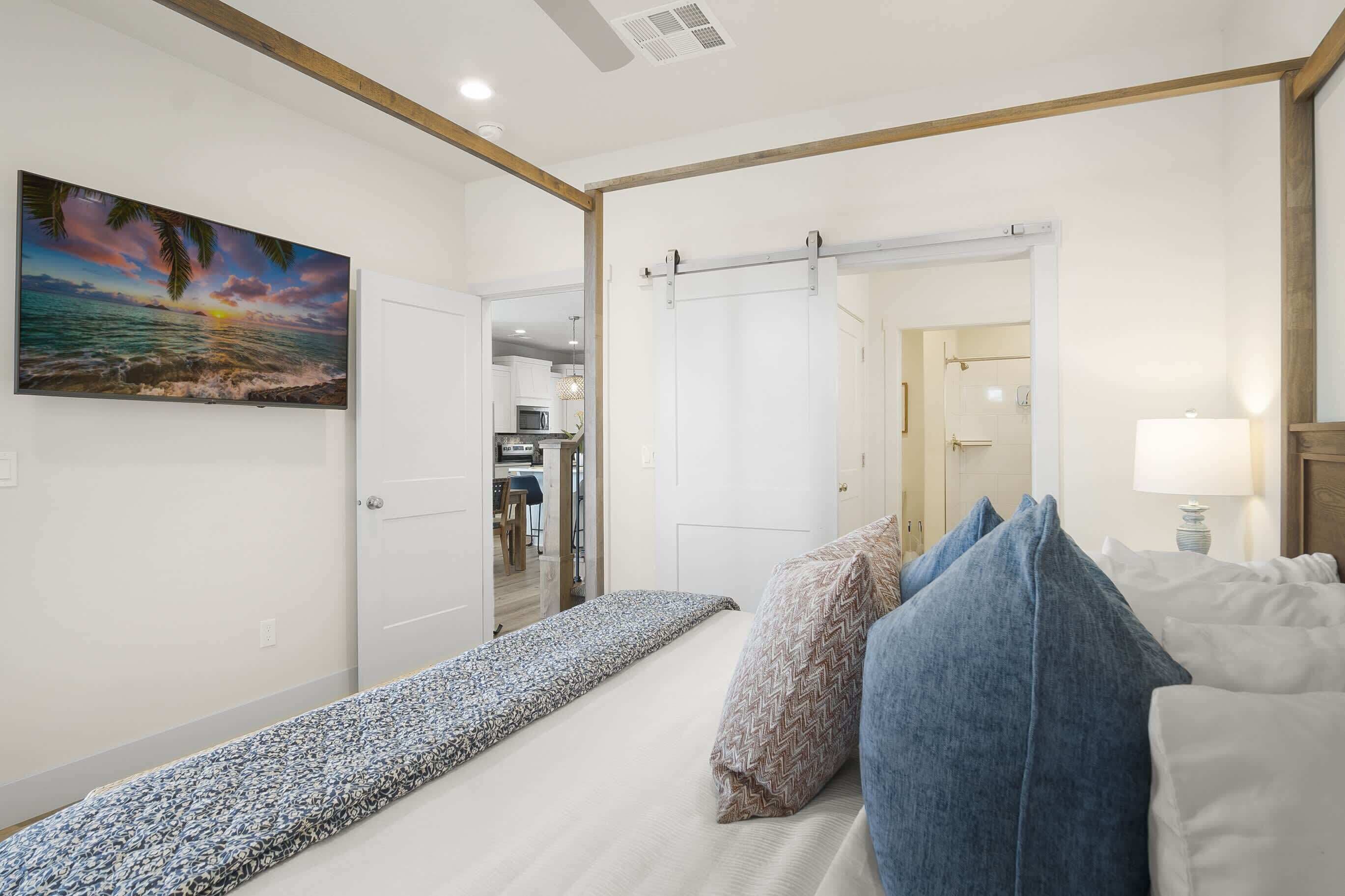A bedroom with a bed, pillows, a painting, and a door leading to a bathroom.