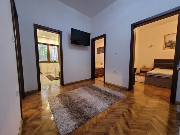 A hallway with wooden flooring, a grey rug, and a flat-screen TV mounted on the wall.