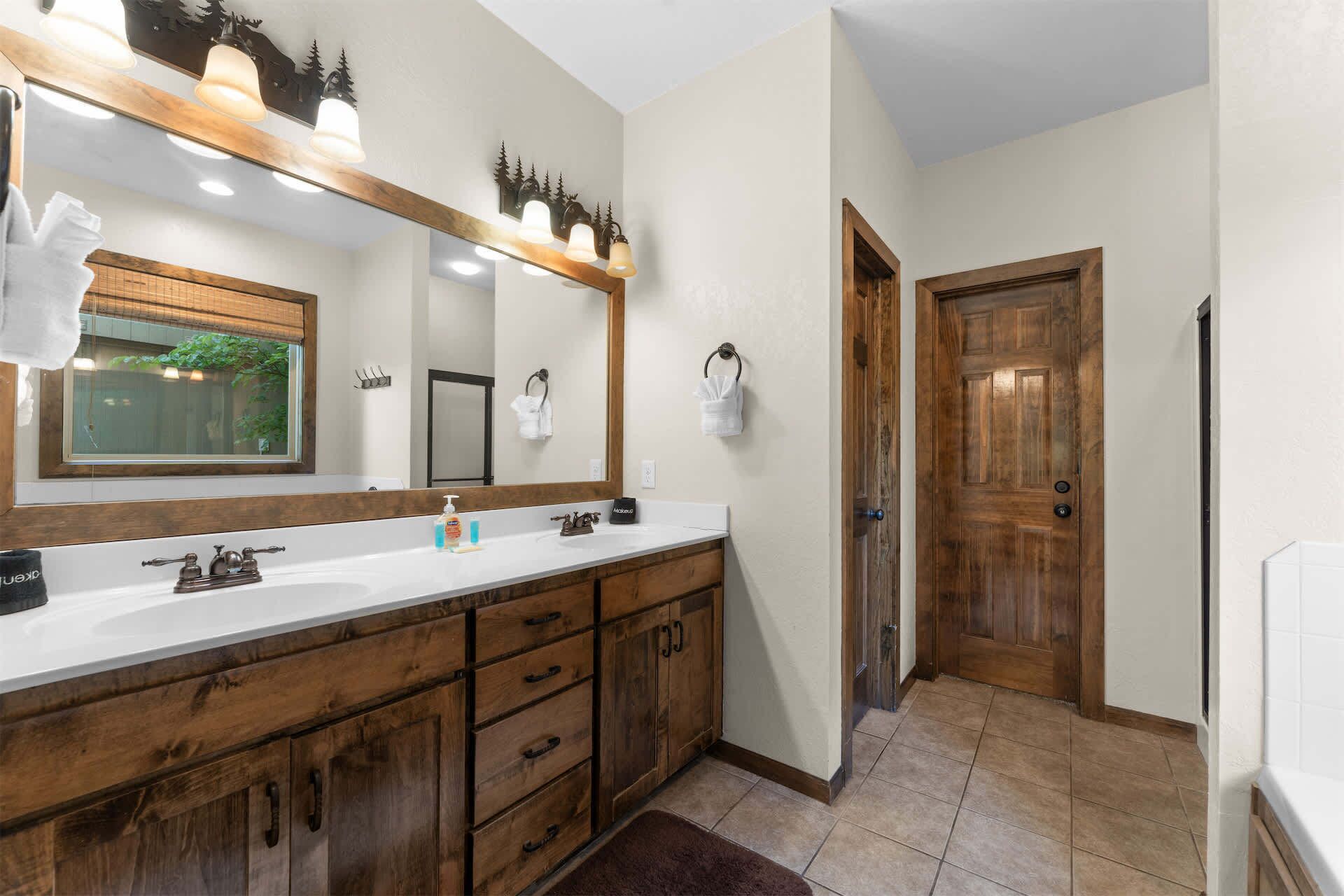 A bathroom with a large mirror, wooden vanity, and a door leading to another room.