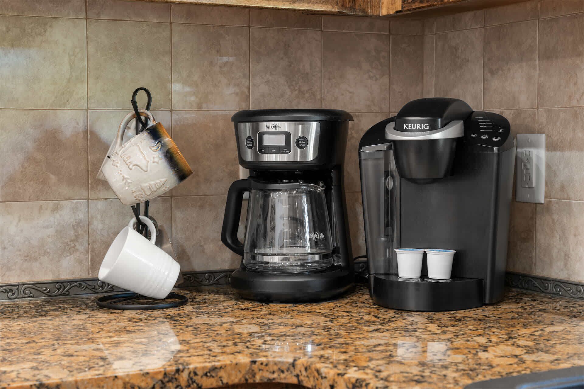 Une machine à café, une bouilloire et deux tasses sur un plan de travail de cuisine.
