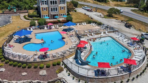 A resort with two swimming pools, a large building, and a road in the background.