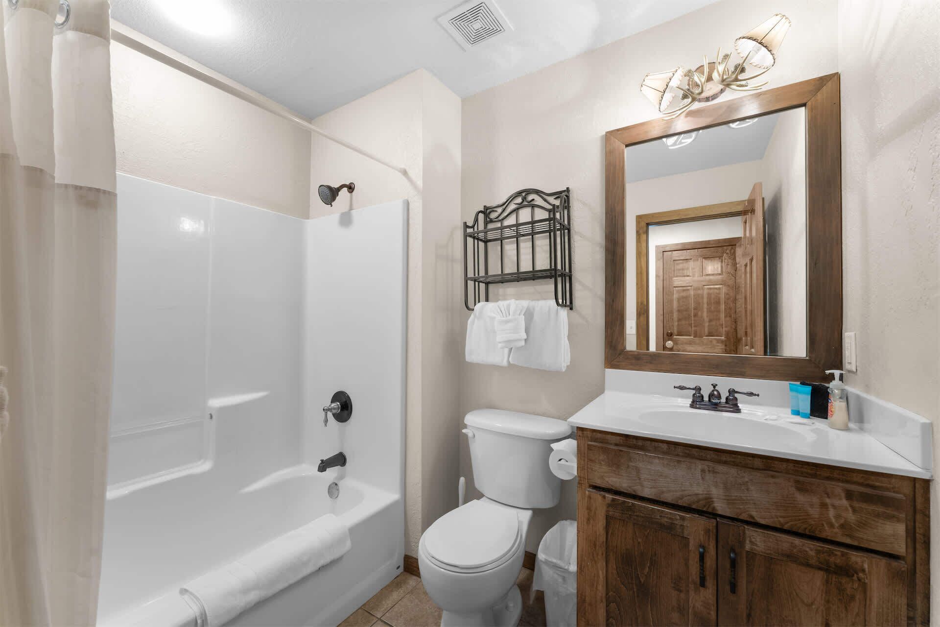 A bathroom with a bathtub, toilet, vanity with wooden cabinets, a mirror, and a towel rack.