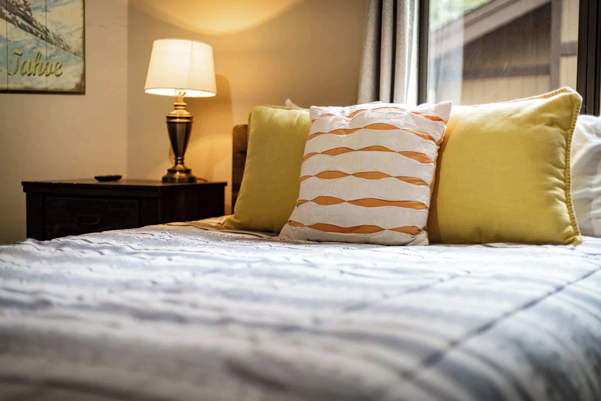 A neatly made bed with patterned pillows, a bedside lamp, and a framed picture on the wall.