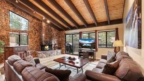 A spacious living room with a stone fireplace, leather sofas, a wooden ceiling, and large windows offering views of the outdoors. - Heavenly Haven - Hot Tub + Seasonal HOA Pool (Zephyr Cove)