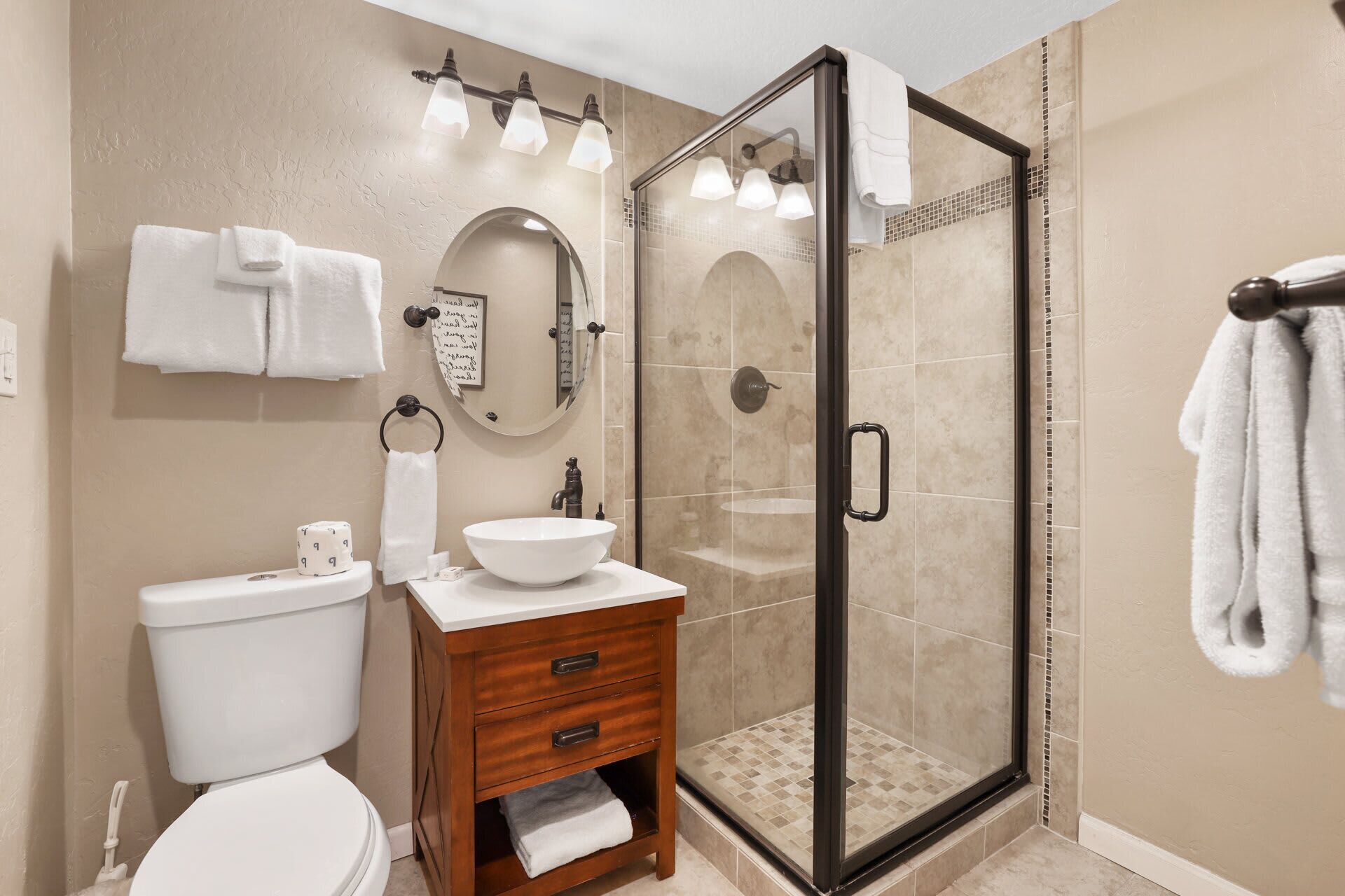 A bathroom with a glass-enclosed shower, a white sink, a wooden vanity, and a toilet.