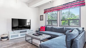 Uma sala de estar moderna com uma televisão de tela plana grande, sofá cinza e uma janela com cortina listrada.