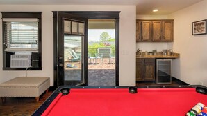 Una mesa de billar en una habitación con una puerta de cristal corredera que da a un patio exterior con sillas y una mesa.