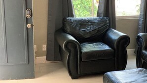 Ein Zimmer mit einem schwarzen Ledersessel, einem kleinen Hocker und einem Fenster mit Vorhängen.