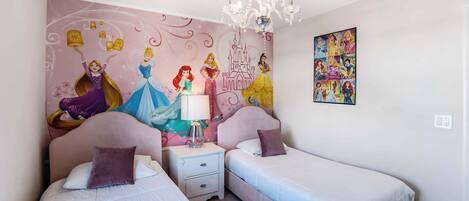 Ett sovrum med två sängar, ett nattduksbord, en kristallkrona och en väggmålning med Disneyprinsessor.