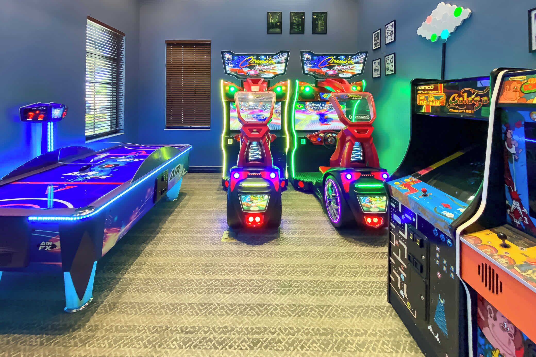 Ein Raum mit Billardtisch, drei Spielautomaten und einem Fenster mit Jalousien.