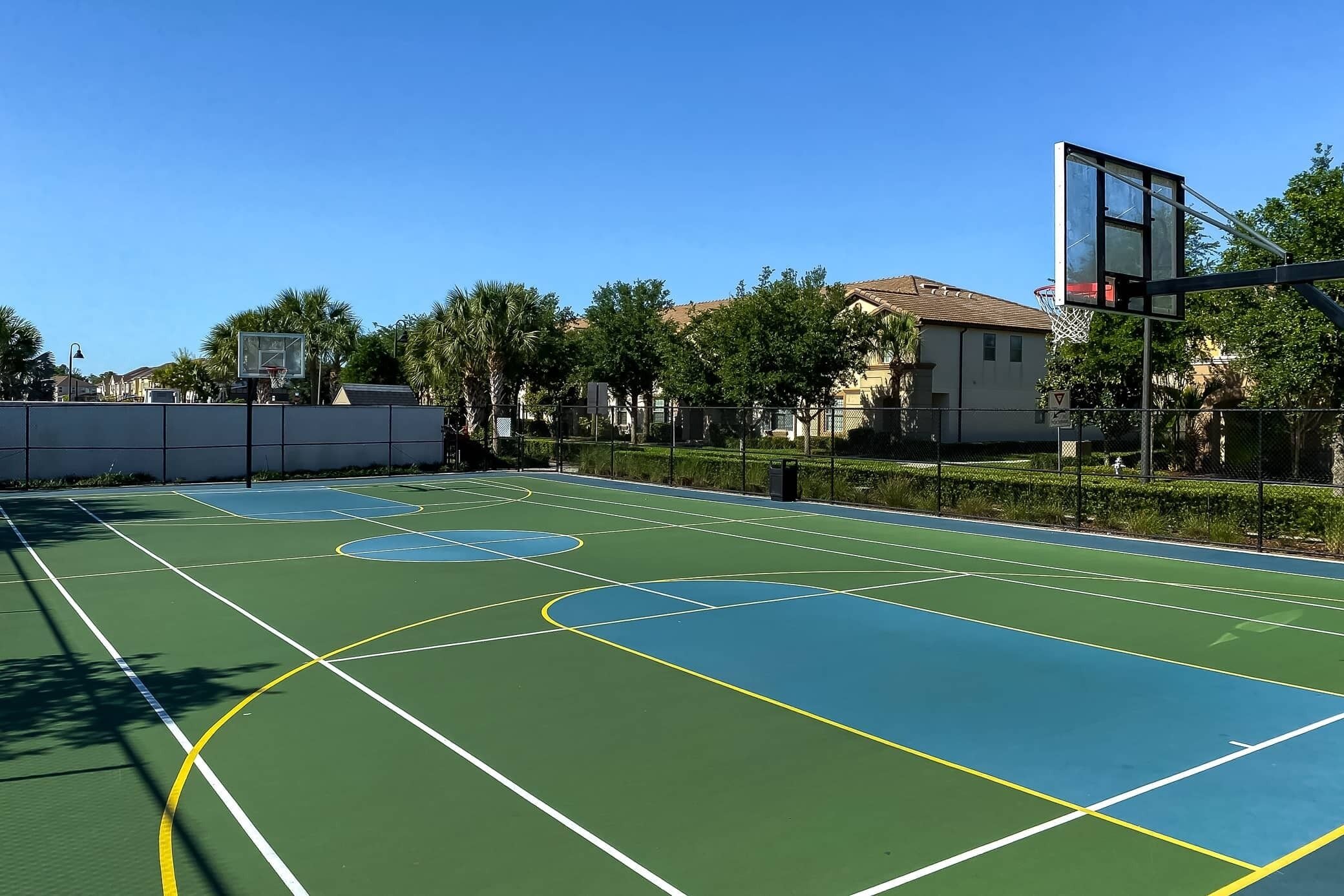 Un terrain de basket en plein air avec des lignes bien définies, un panier et une clôture en treillis métallique.