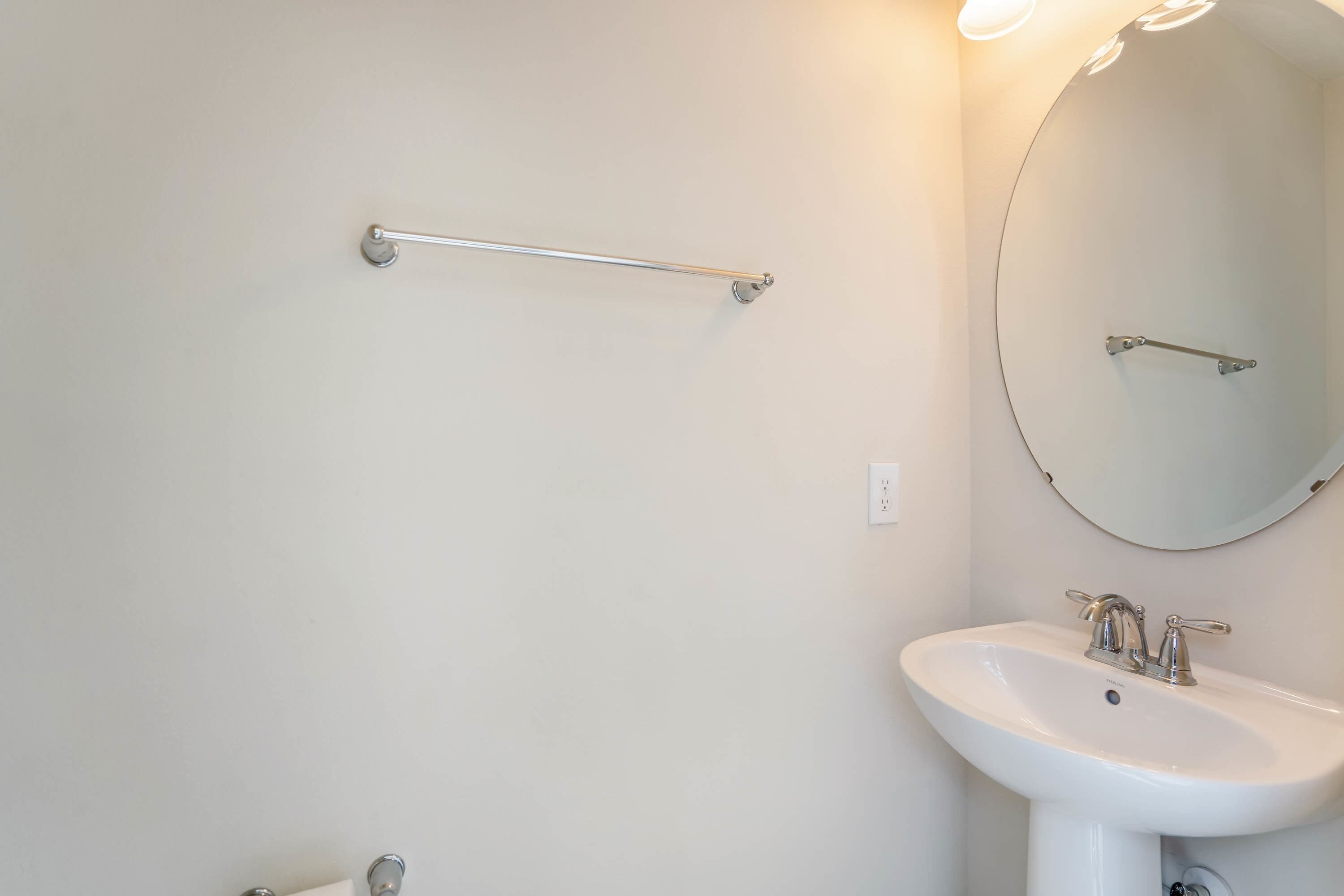 A bathroom with a white sink, a mirror, and a grab bar on the wall.