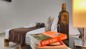 Una cama bien hecha con una manta marrón, una toalla enrollada y un libro titulado "Costa Rica" sobre una mesita de noche de madera.