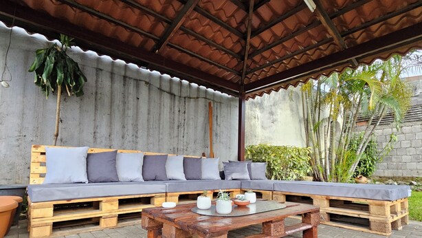 Un espacio al aire libre cubierto con un banco de madera y una mesa, rodeado por un muro de metal corrugado y plantas en macetas.