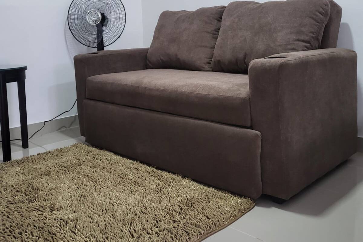 A living room with a brown sofa, a standing fan, a small table, and a beige rug.