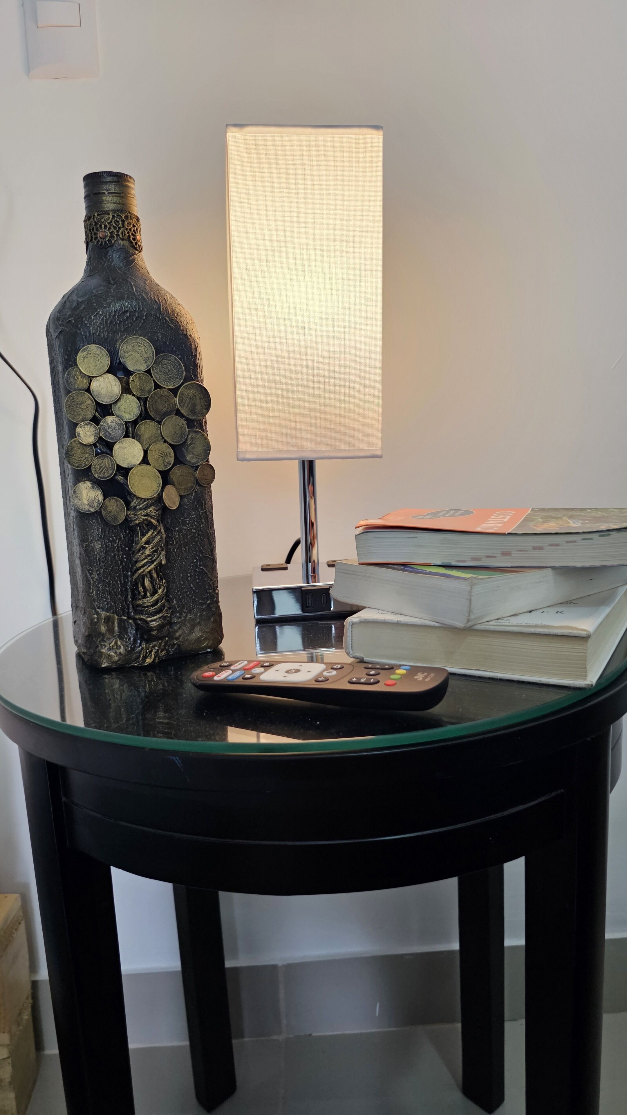 A glass table with a decorative bottle, a lamp, and a stack of books.