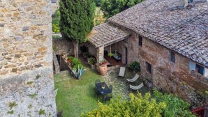 A stone building with a tiled roof, a covered patio with outdoor seating, and a stone wall. - Torre 2 by Interhome (Sovicille)