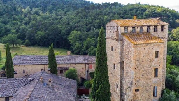 A stone building with a tower, surrounded by trees and a hilly landscape. - Torre 2 by Interhome (Sovicille)