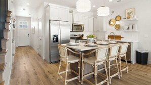 Une cuisine moderne avec des meubles blancs, des appareils en acier inoxydable et un coin repas doté de chaises en osier.