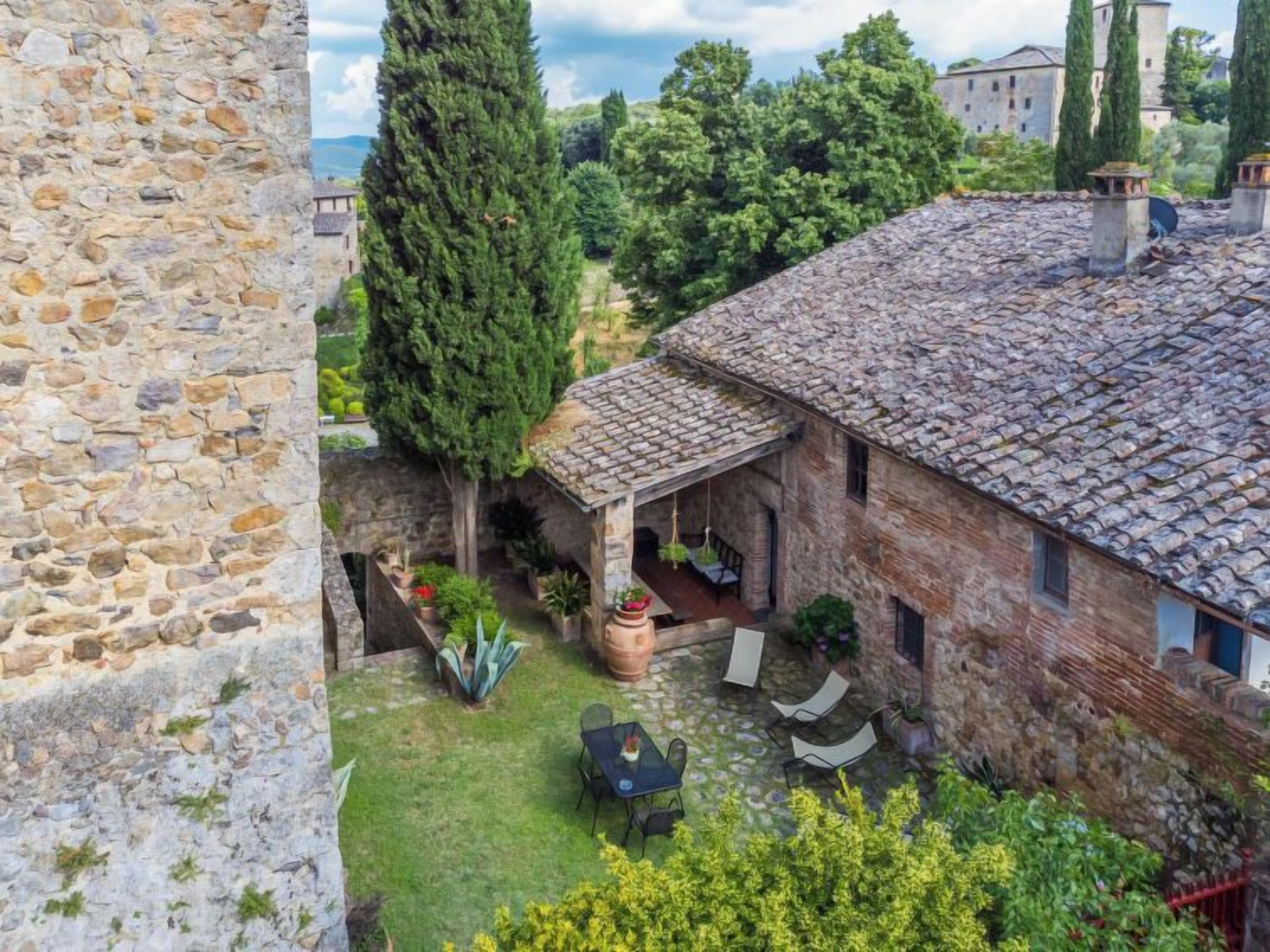 A stone building with a tiled roof, a covered patio with outdoor seating, and a stone wall.