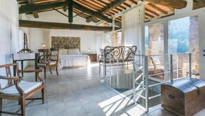 A spacious room with a high ceiling, exposed wooden beams, a bed with a headboard, a desk with a chair, a metal-framed balcony, and a large window. - La Torre by Interhome (Sovicille)