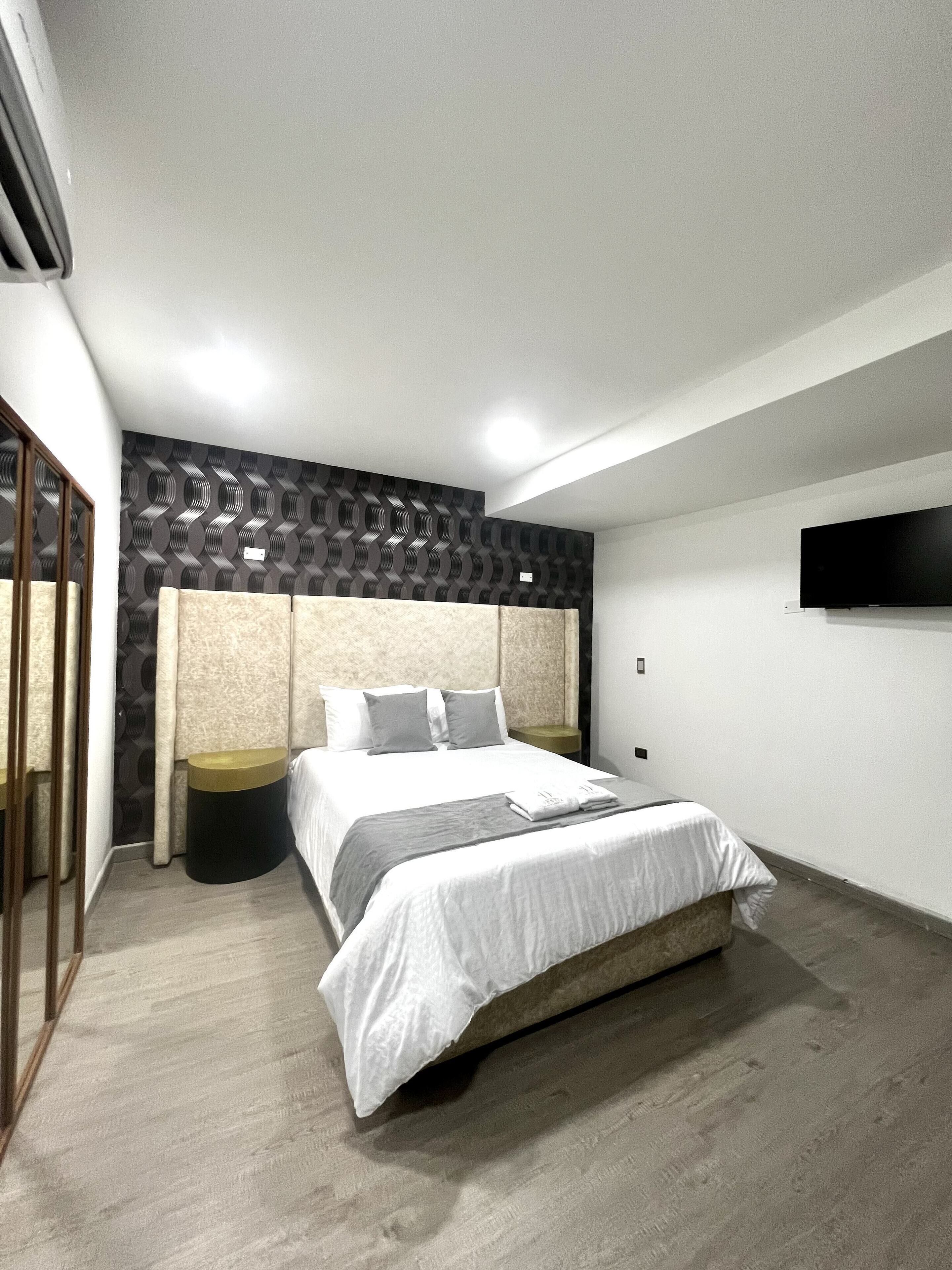 Ein modernes Schlafzimmer mit einem großen Bett, einem an der Wand befestigten Fernseher und einer Wandgestaltung mit Muster.